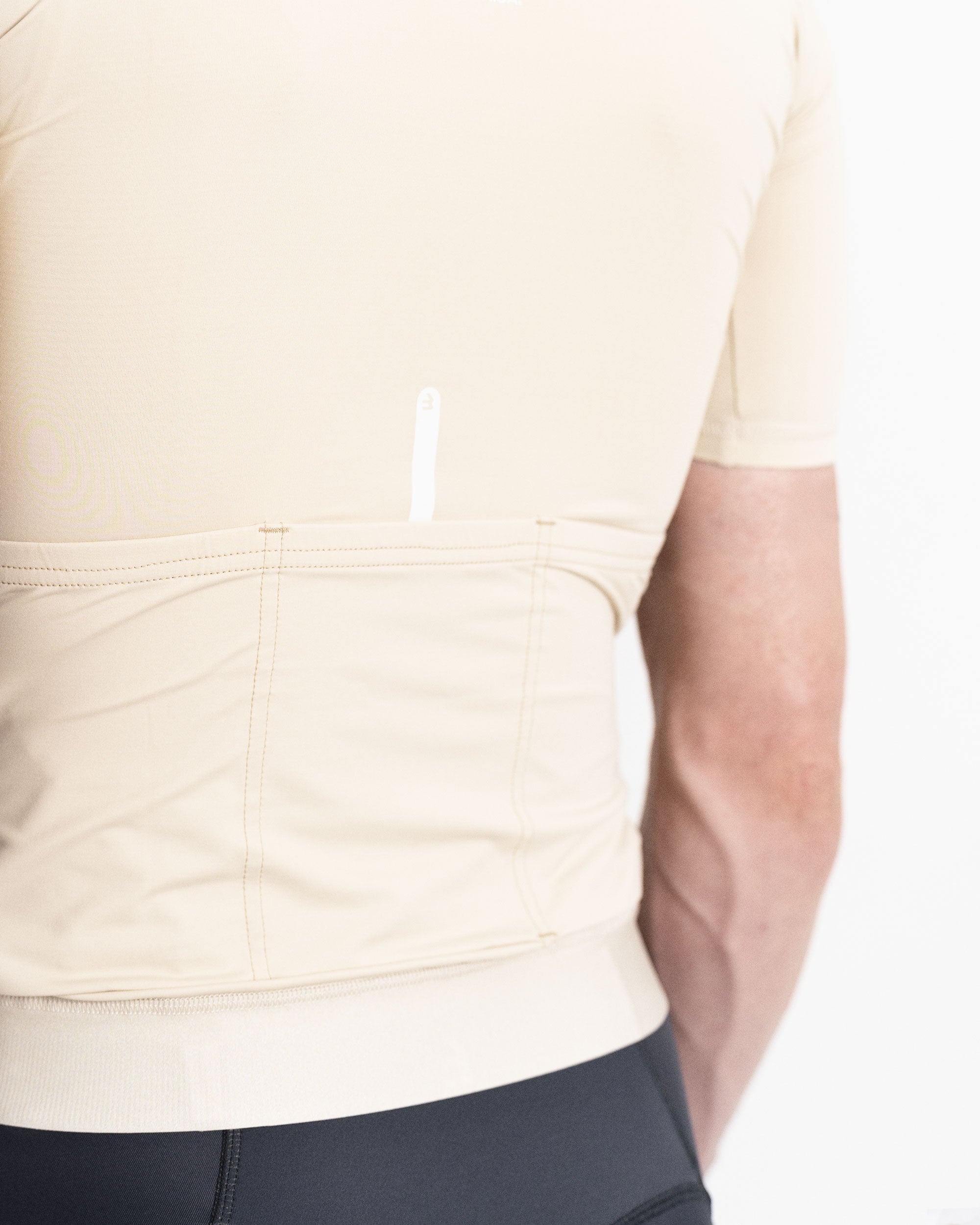 Imagen de detalle de maillot de ciclismo de hombre crema de la parte trasera. Se puede ver una línea reflectante en blanco que sale del bolsillo trasero. 3 bolsillos de alta capacidad en la zona lumbar.